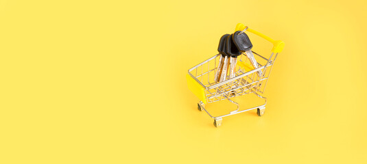 Fototapeta na wymiar Mini cart with keys on a yellow background. The concept of buying or renting a house, apartment. copy space for text. Baner. view from above 