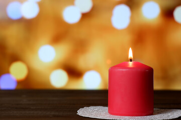 Burning thick pink aromatic candle on white openwork paper napkin on wooden table, yellow bokeh lights background closeup view selective focus. Love, Valentine's, women's day, romantic concept