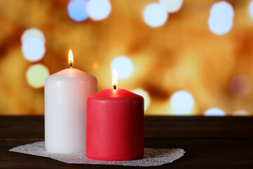 White and pink burning aromatic candles on white openwork paper napkin on wooden table, yellow bokeh lights background closeup view selective focus. Love, Valentine's, women's day, romantic concept