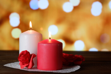 White and pink burning aromatic candles and roses on white openwork paper napkin on wooden table, yellow bokeh lights background selective focus. Love, Valentine's, women's day, romantic concept