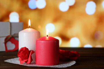 White and pink burning aromatic candles, roses, gift on white openwork paper napkin on wooden table, yellow bokeh lights background selective focus. Love, Valentine's, women's day, romantic concept