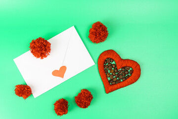 Red heart and coffee beans inside next to a white envelope and red pompoms on a green background.