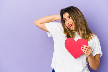 Young indian woman holding a valentines day heart isolated touching back of head, thinking and making a choice.