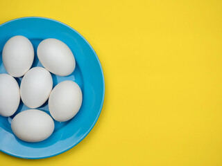 White eggs on a blue plate on a yellow background.