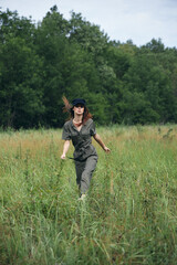 Naklejka na ściany i meble Woman on nature In a green jumpsuit, a black cap is a tall grass landscape 