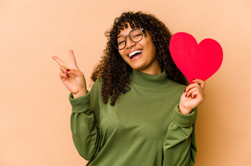 Young african american afro woman holding a valentines day heart joyful and carefree showing a peace symbol with fingers.