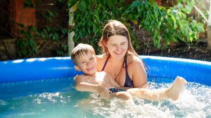 Happy smiling mother holding and supporting her little son learning to swim in inflatable swimming pool. Family summer vacation and holidays