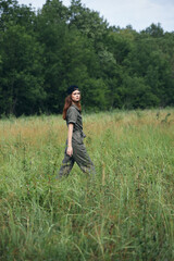 Naklejka na ściany i meble Woman in the meadow Nature walks through the field against the background of trees 
