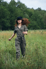Naklejka na ściany i meble Woman in the field Green jumpsuit black cap jogging on the grass 