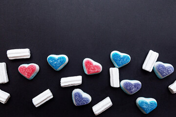 Colored gummy hearts and marshmallows on a black background. Sweet background for valentine's day