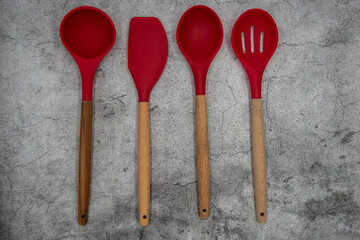 Various kitchen tools made of red silicone and wood on a concrete work surface