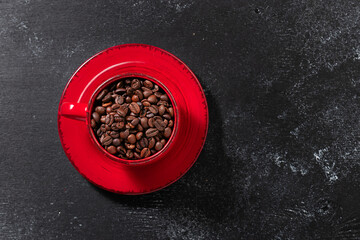 Minimalism style composition with red cup with aromatic coffee beans on black rustic background with copy space for your design. Coffee shop or cafeteria promo banner template.