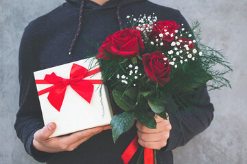 Man holding a bouquet of red roses and gift box in his hand for Valentine's Day