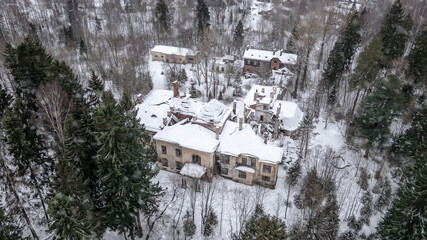An old abandoned manor house in a snowy forest. Abandoned building. Snowy day. Tall trees.
