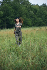 Naklejka na ściany i meble Woman in the meadow running on tall grass in green jumpsuit 