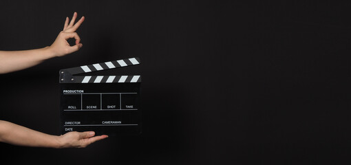 Hand is holding Black clapper board or movie slate on black background.Other hand do A ok or okay...