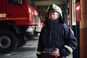 Male firefighter in protective uniform standing near truck