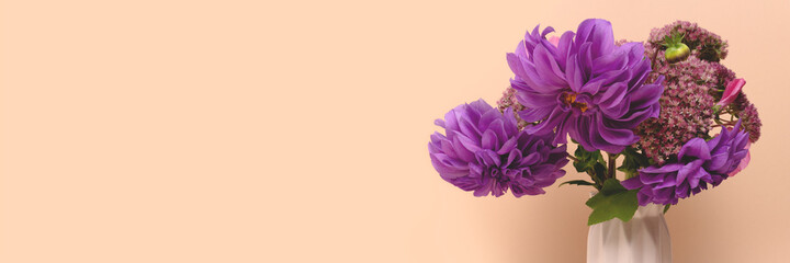 Banner with bouquet of purple dahlia flowers in vase in front of beige background. Springtime floral composition with copyspace.