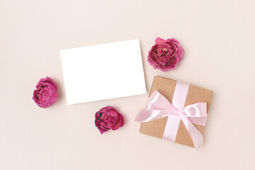 Greeting card mockup, gift box and rose flowers on a beige background. Festive romantic concept with copyspace.