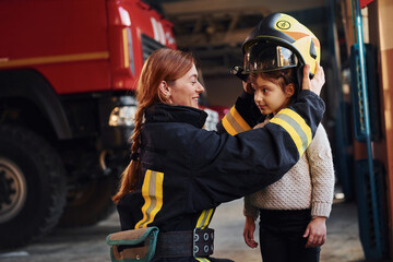 Happy little girl is with female firefighter in protective uniform