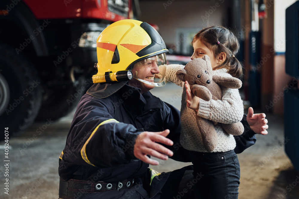 Wall mural happy little girl is with male firefighter in protective uniform