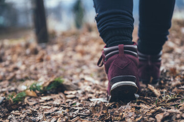 Legs in dark red, plum, sport, walking boots in the forest surrounded by leaves.