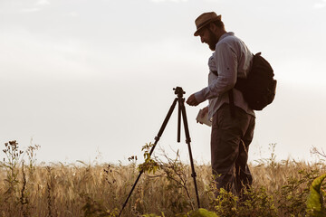 a surveyor with a beard set up a tripod on the field