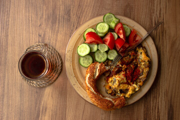 Traditional Turkish tea in tea glass and Turkish bagel, tomato slices, cucumber slices in the plate on a wooden table. Turkish breakfast, alone breakfast,Sunday breakfast or office breakfast.
topview.