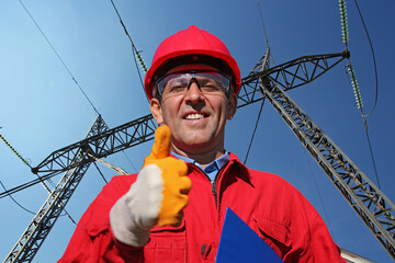 Electric Utility Worker Giving Thumbs Up Next to Electrical Transmission Tower