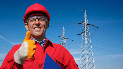 Smiling Electric Utility Worker Giving Thumbs Up Next to Electrical Transmission Towers