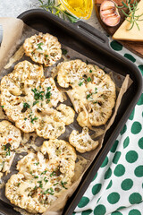 Baked cauliflower with cheese, garlic, herbs, and spices in a baking sheet. Top view. Tasty vegetarian food.