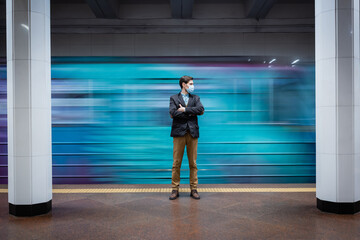 motion blur of man in medical mask standing with crossed arms near passing wagon in subway