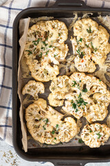 Baked cauliflower with cheese, garlic, herbs, and spices in a baking sheet. Top view. Tasty vegetarian food.