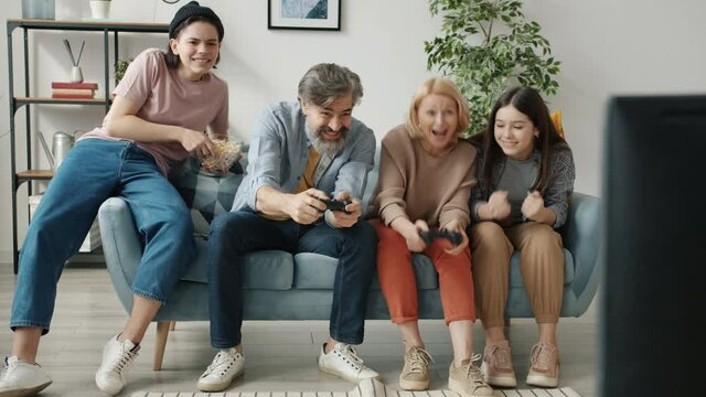 Happy family mom and dad playing videogame enjoying leisure time together bonding with teenage children. Gaming and modern lifestyle concept.