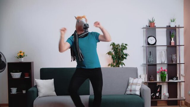 In the room, a man dances in a horse mask, spreading his arms to the sides.