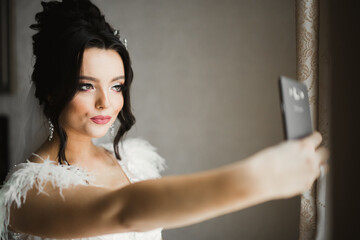 A sweet smiling bride in a light interior makes selfie on the phone