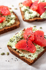 Toasts with rye bread, avocado, cottage cheese, grapefruit, and pumpkin seeds close-up. Tasty and healthy breakfast or snack. Vegetarian food.