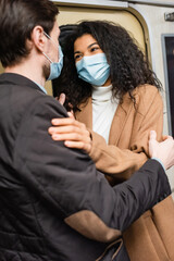 african american woman in medical mask hugging with boyfriend in subway