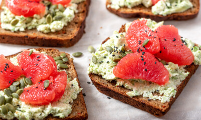 Toasts with rye bread, avocado, cottage cheese, grapefruit, and pumpkin seeds close-up. Tasty and healthy breakfast or snack. Vegetarian food.