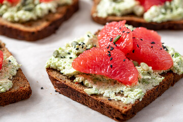 Toasts with rye bread, avocado, cottage cheese, grapefruit, and pumpkin seeds close-up. Tasty and healthy breakfast or snack. Vegetarian food.
