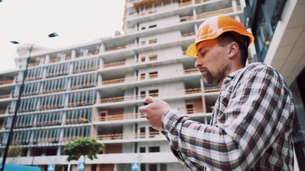 Acceptance of construction works. A man in a hard hat holds a construction plan in the phone. The man checks the conformity of the building structure. Assessment of the quality of construction