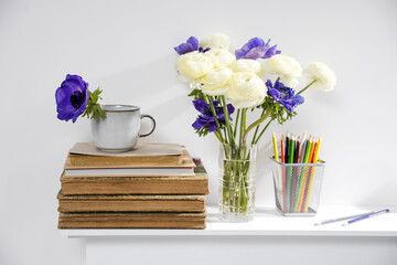 One blue anemone in a multi-colored vase in the style of the seventies on the table with books as an interior decoration.