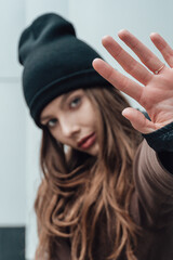 Selective focus portrait of young female model in hipster style hat and coat showing denial gesture with her hand.