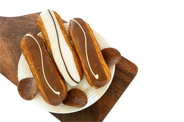 On a white plate are three custard eclairs with chocolate and vanilla glaze and pieces of milk chocolate.