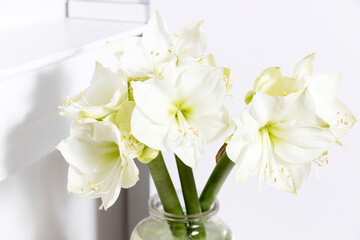 Bouquet of white lilies in a tall glass vase on a beige table against a gray wall. Copy space.