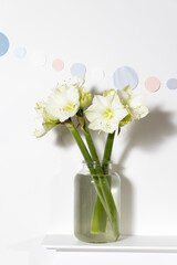 Bouquet of white lilies in a tall glass vase on a beige table against a gray wall. Copy space.