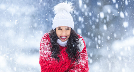 Good-looking woman in red sweater smiles at the camera while being cold outside on a snowing winter day.