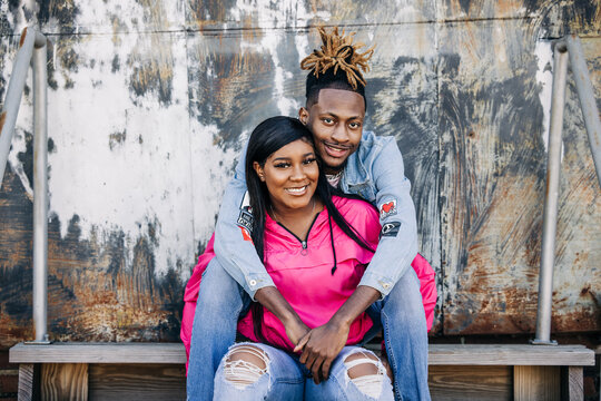 An attractive and fun African-American couple sitting outside on steps in an urban setting with a jacket and denim jeans hanging out and having fun and spending time together - Powered by Adobe