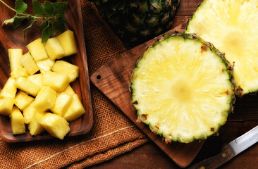 High angle shot of a fresh cut pineapple with knife on cutting board. Slices and a plate full of diced sections.