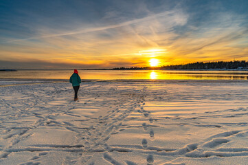 The lonely female traveller enjoying the beautiful view of sunset on a sea beach covered by snow